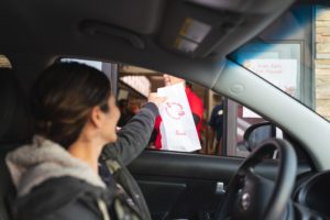 View of a person being handed a bag of fast food at a drive-through from the perspective of a passenger in the vehicle.